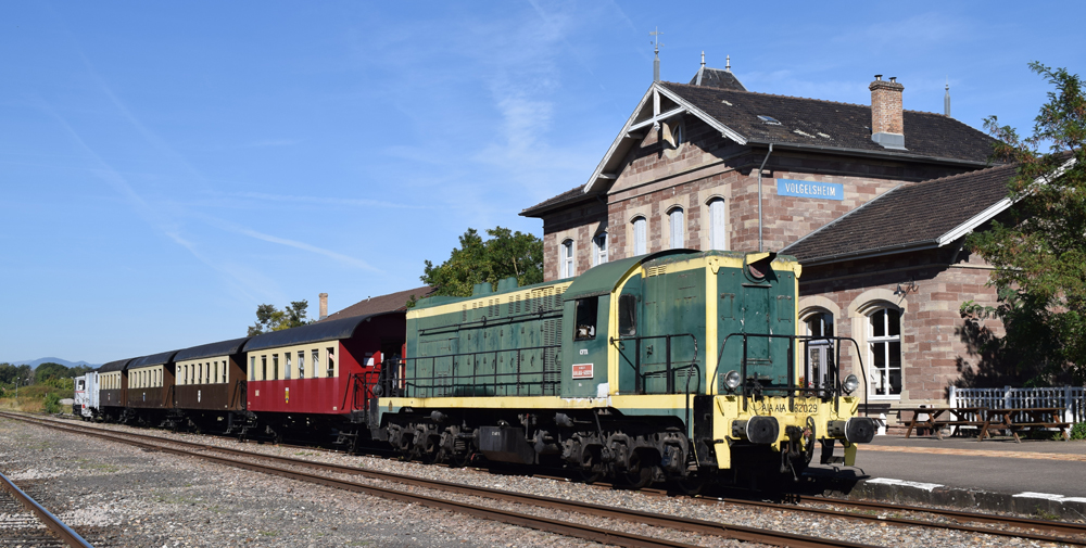 Green and yellow diesel with passenger train in front of station