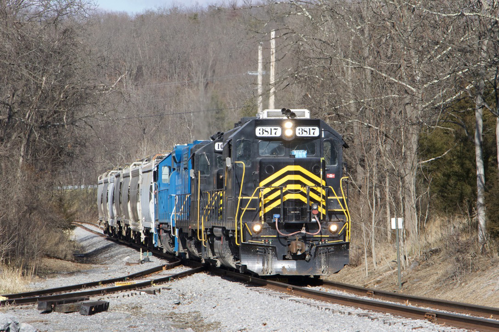 Train with black and yellow locomotive leading and several covered hoppers