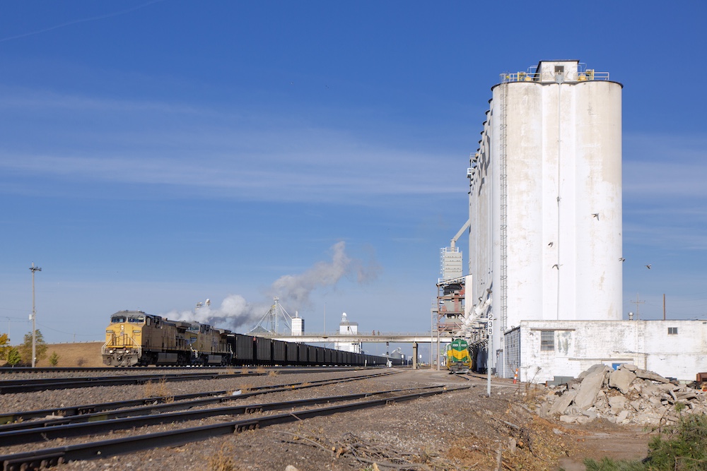 A yellow coal trail passes a white grain elevator