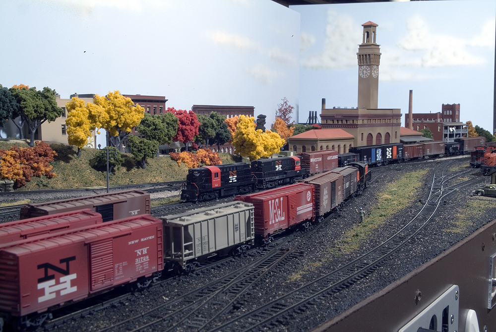 Freight cars from Northeastern railroads fill the yard of an N scale layout with autumn trees and brick buildings in the background