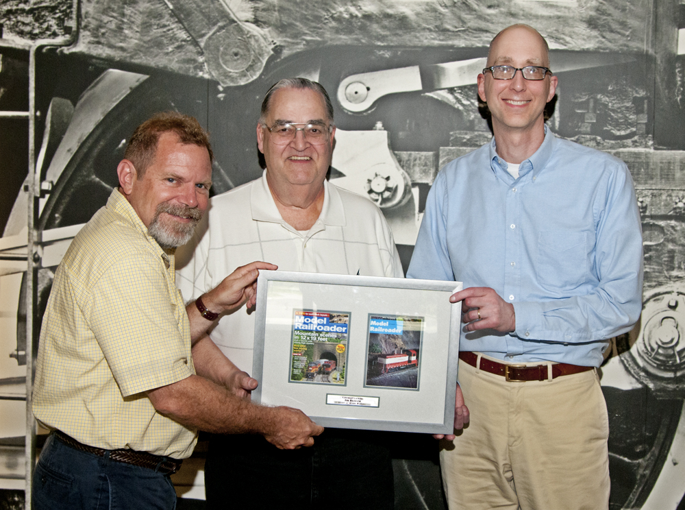 Color photo of three men holding an award.