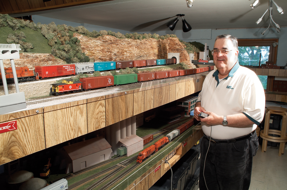 Color photo of man holding a throttle running a model railroad.