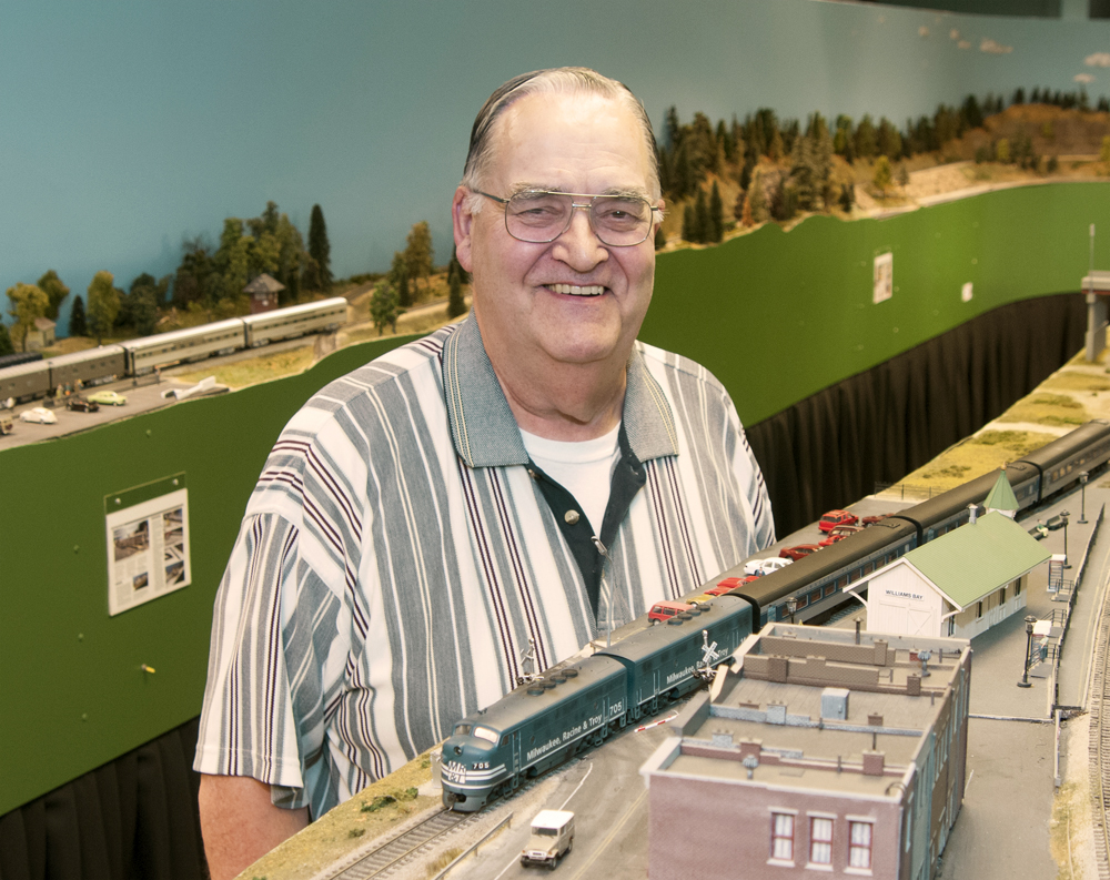 Photo of man standing by HO scale model railroad. 