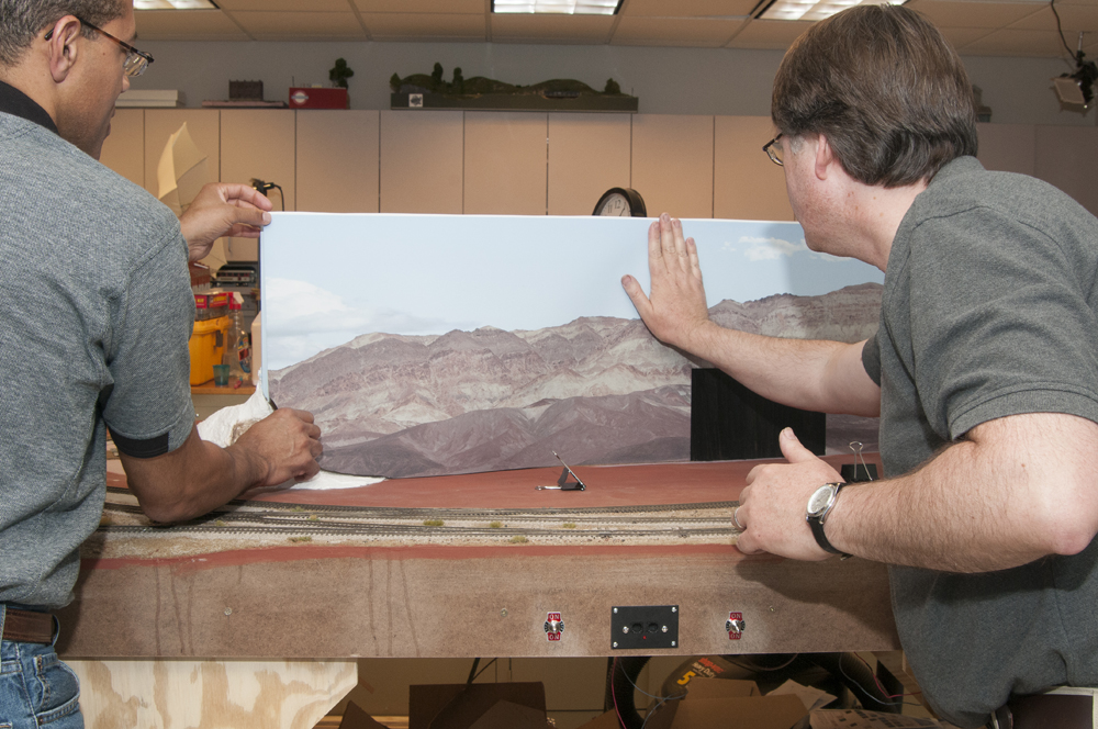 Photo of two men applying backdrop to HO scale layout.