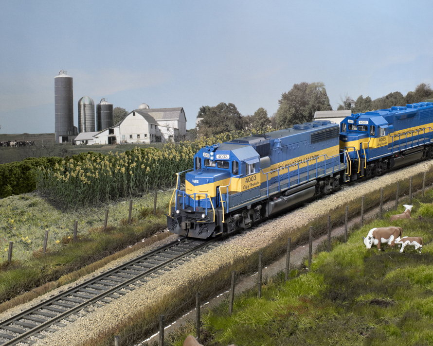 Photo of two blue-and-yellow HO scale diesels passing a farm scene.