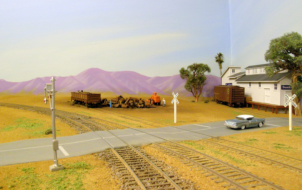 Color photo of HO scale layout with vehicle, building and two freight cars in scene.