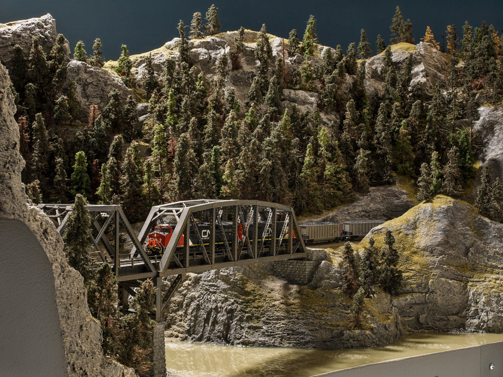 Color photo of N scale train crossing bridge in rugged mountain terrain.