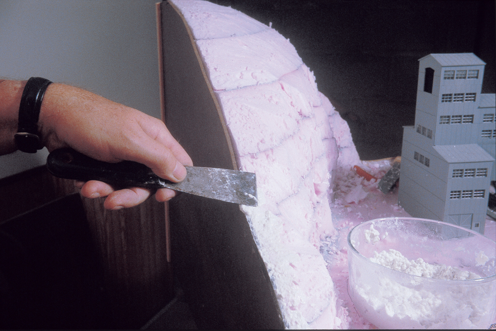 Photo of man applying Sculptamold to pink extruded-foam insulation board with putty knife.
