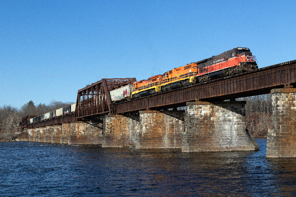 Freight train with three diesel locomotives crossing a bridge.