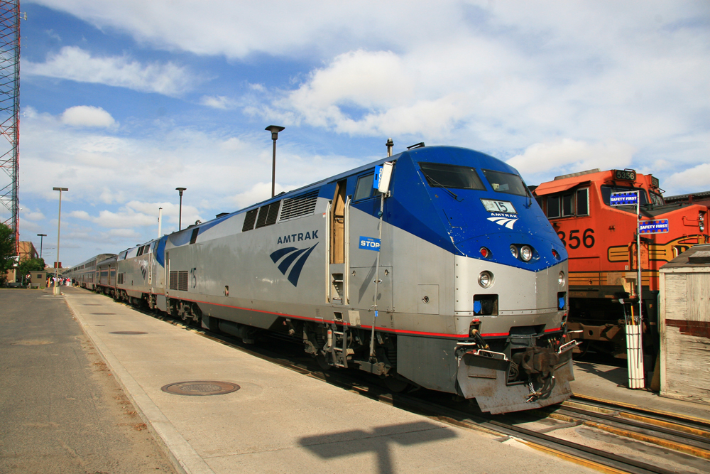 Locomotive on passenger train carrying blue maintenance flags during station stop