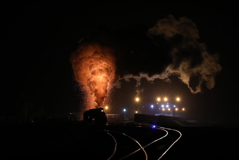 Plume of smoke from steam locomotive illuminated by sparks at night