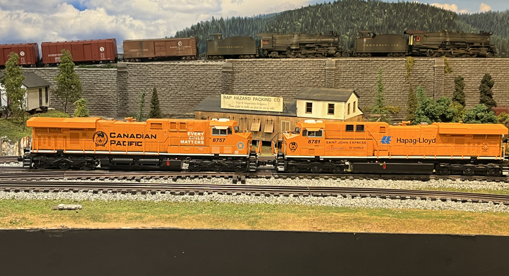 two orange model trains on layout with steam engine on track above