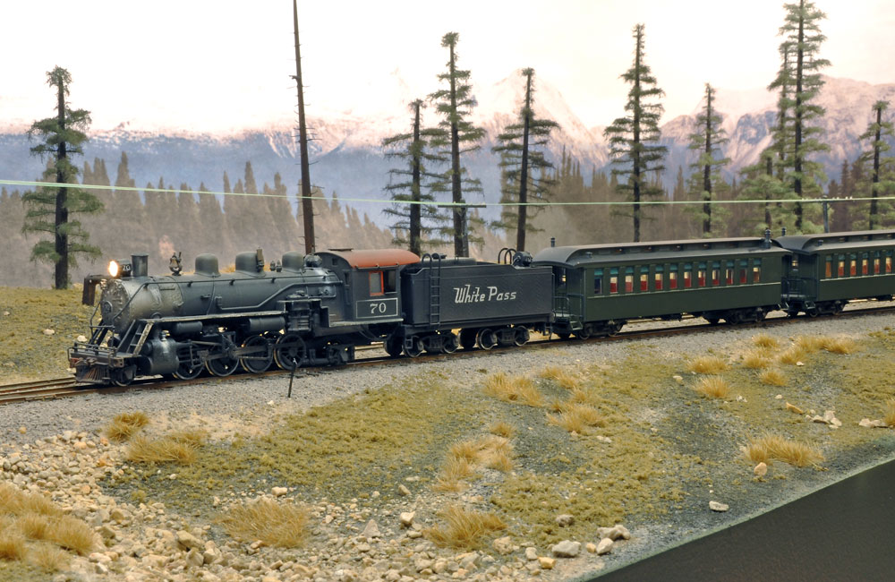 A steam locomotive pulls an old-time passenger train on an HO scale layout