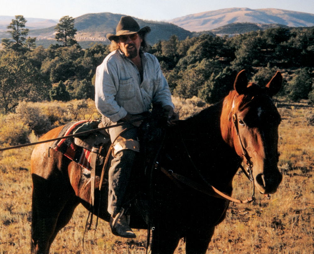 Color photo of man wearing sunglasses and cowboy hat on horse