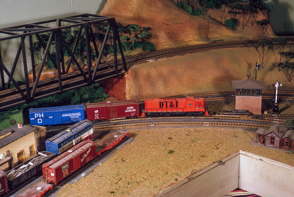 Color photo of a train passing under a bridge near an interlocking tower.