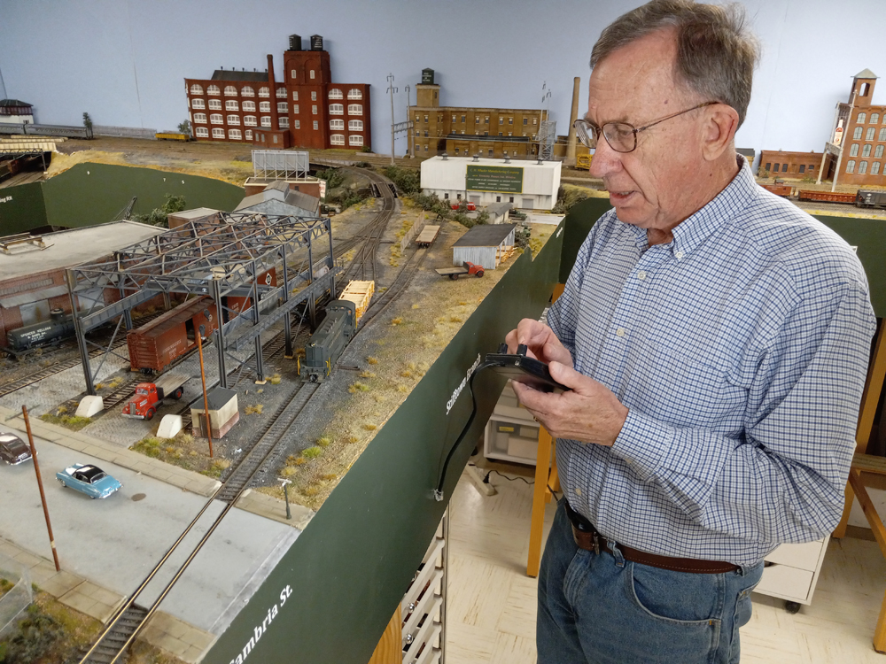 man standing next to model train layout, holding controller