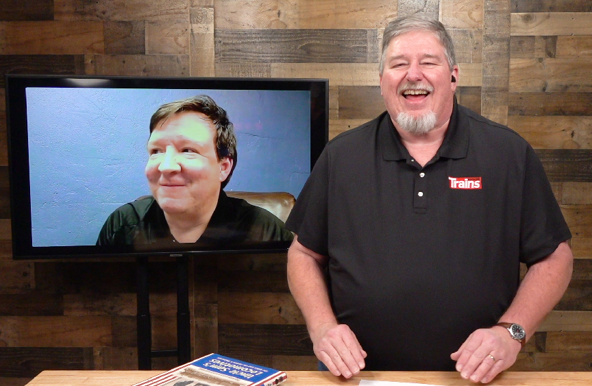 Man in TV studio with interview guest on a video monitor. Trains LIVE — Mikados