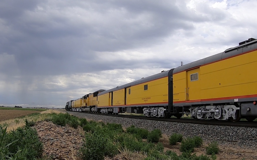 Yellow baggage car right behind a steam and diesel locomotive during a mainline steam excursion.