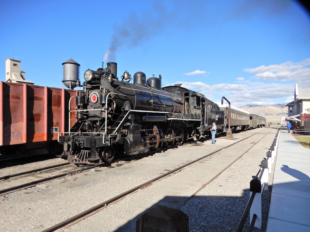 A black steam locomotive leads green passenger coaches