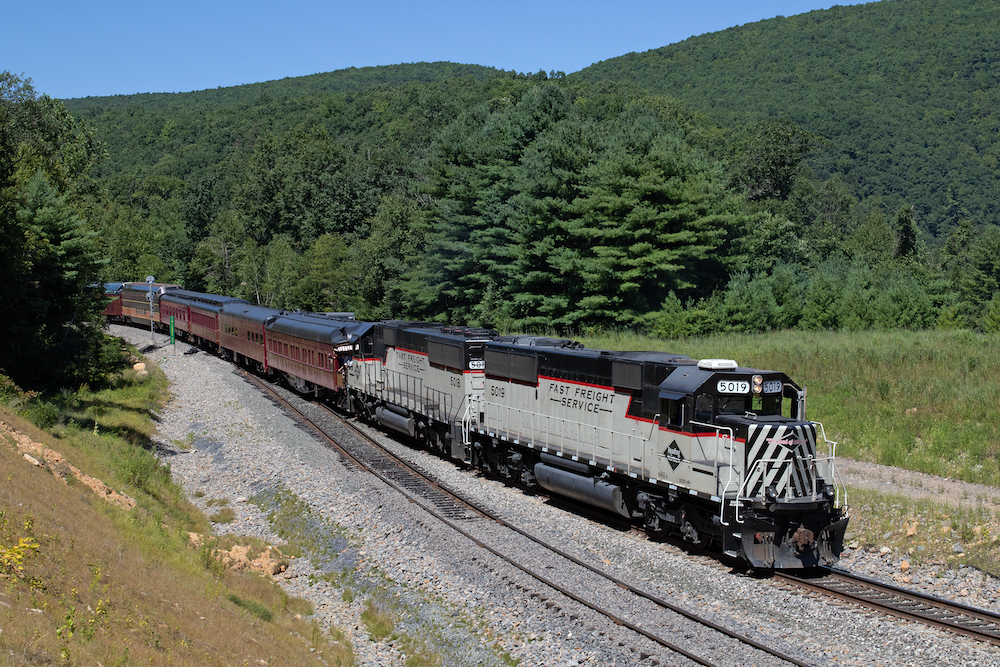 Two diesel locomotives pulling a passenger train through a mountainous terrain.