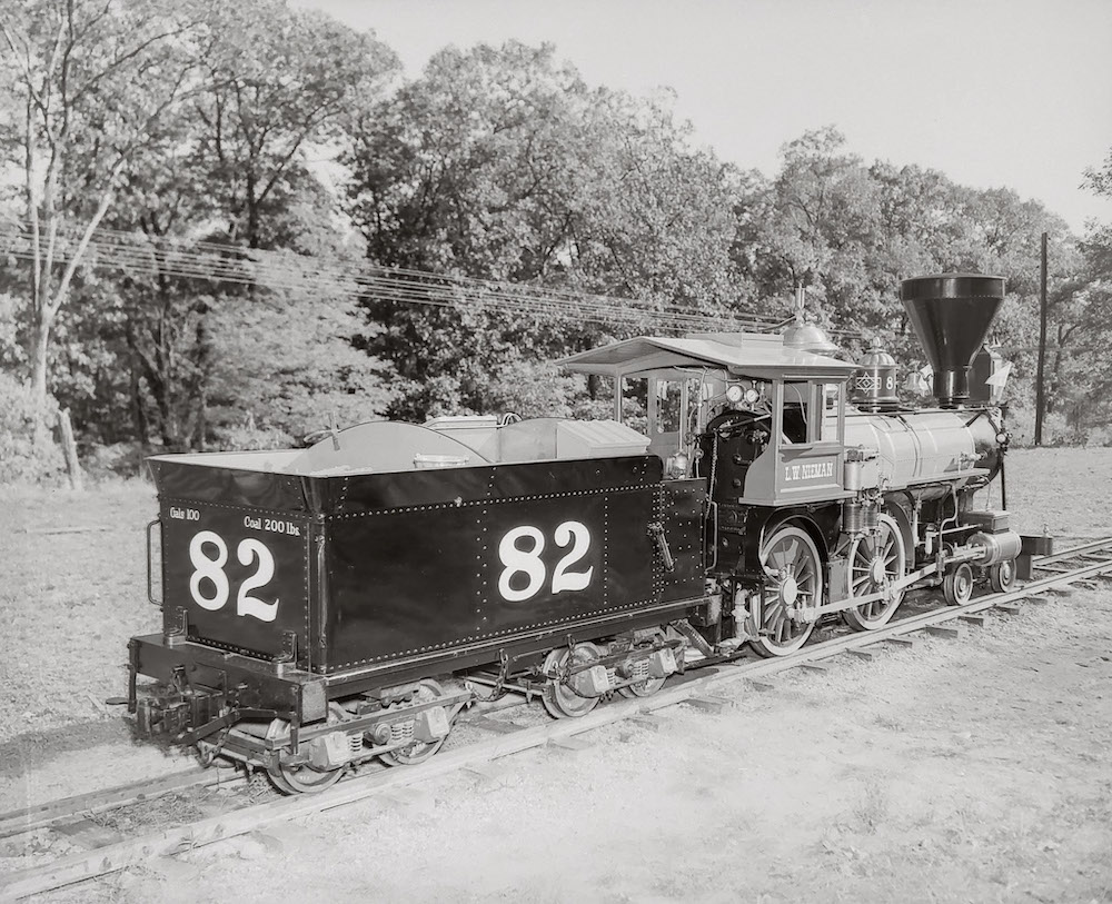 Black-and-white photo of grand-scale 4-4-0 steam locomotive in front of a shop building. The first to receive a homecoming after departing from the Milwaukee County Zoo.