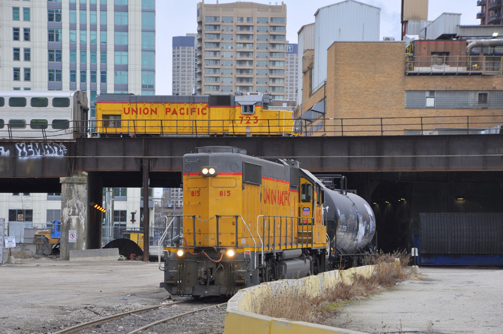 Local switches factory while locomotive moves commuter railcars on overpass