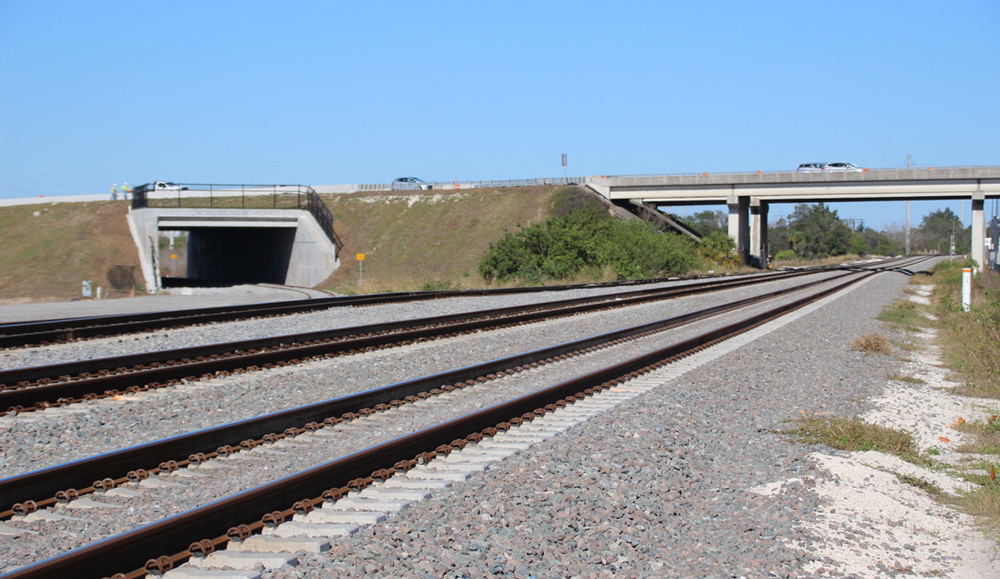 Railroad tracks in foreground with line curving off under highway in background