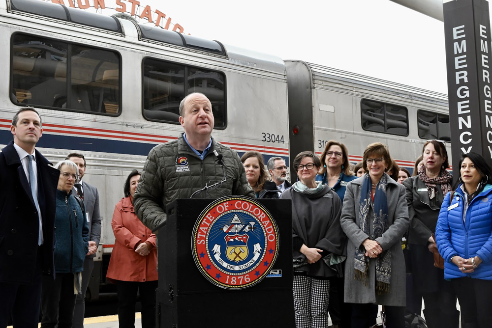 Man speaking at podium with passenger train in background