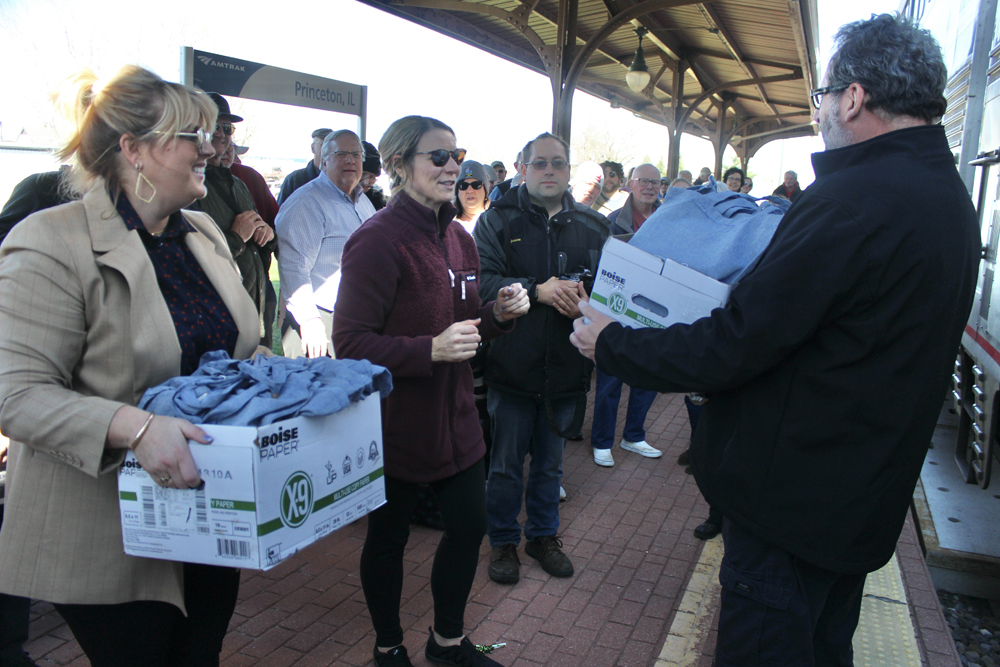 Women give two boxes of tote bags to Amtrak employee at station