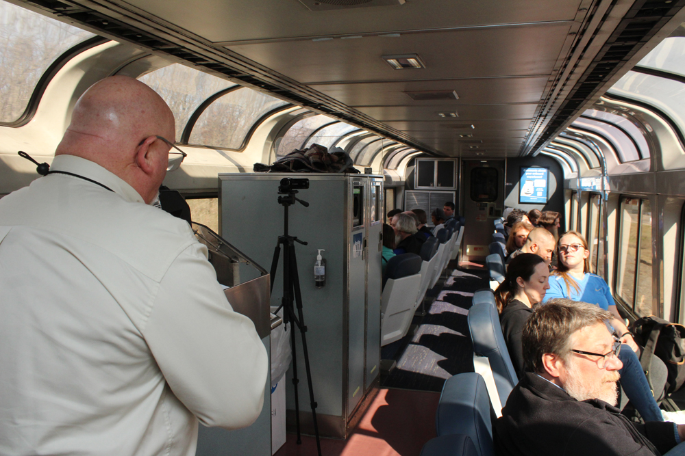 Man speaking into microphone in lounge car of passenger train