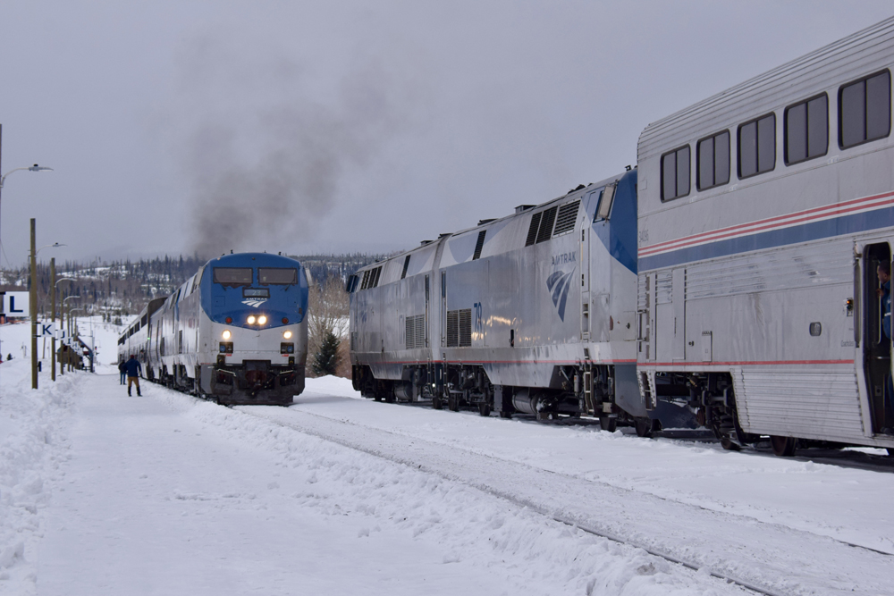 Two passenger trains with bilevel equipment meet in snow