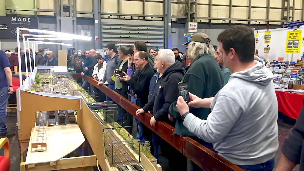 Crowds of people observing a model railroad layout at a large venue.