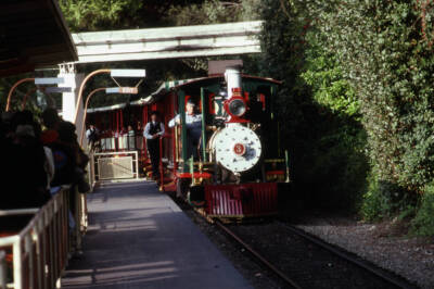 Small steam locomotive leaving passenger station.