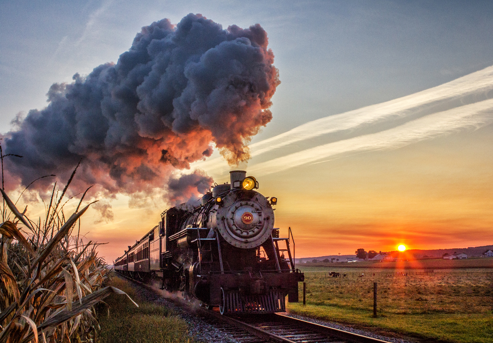 locomotive with steam cloud in front of sunrise