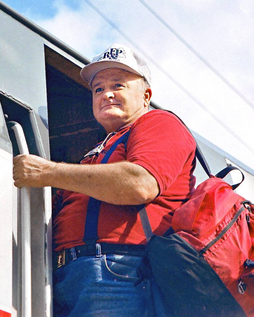 A man in a white cap and red shirt stands in the doorway of a locomotive