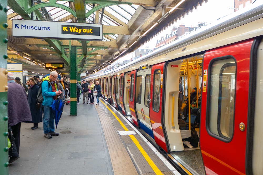 A London tube train waits with open doors under a glass-roofed train shed
