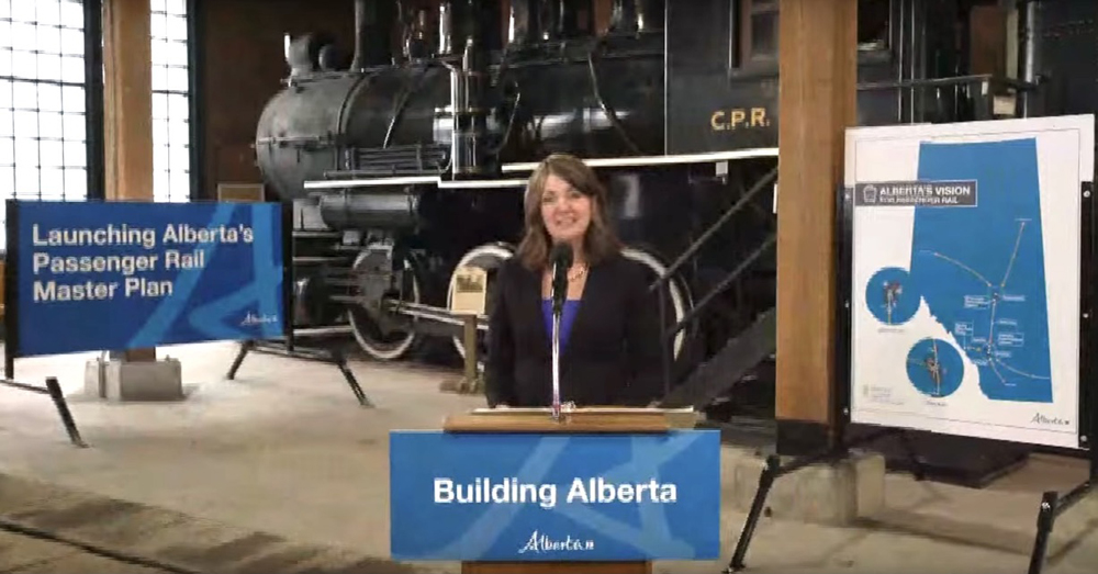 Woman speaking at podium in front of steam locomotive