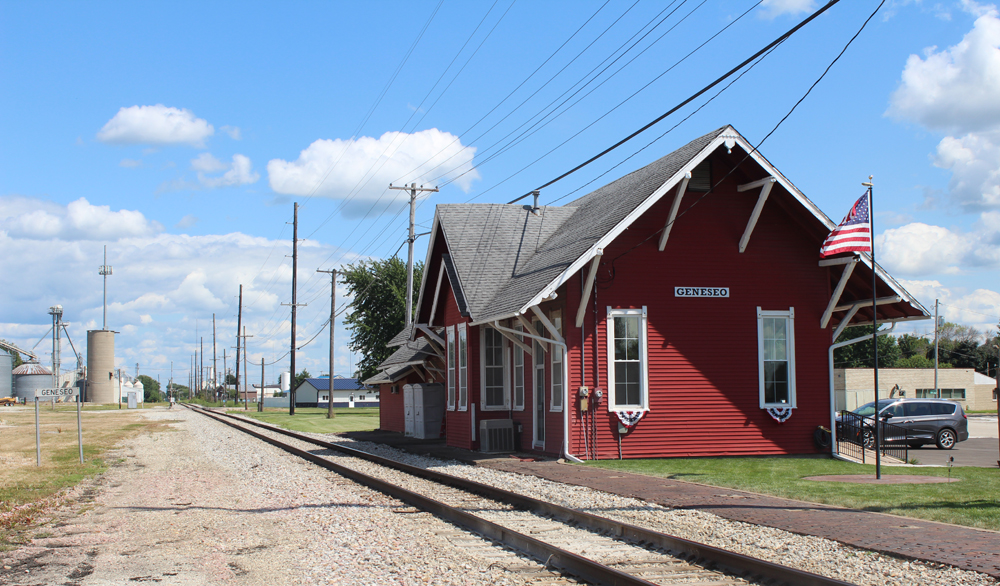 Red wooden railroad station next to single-track line.