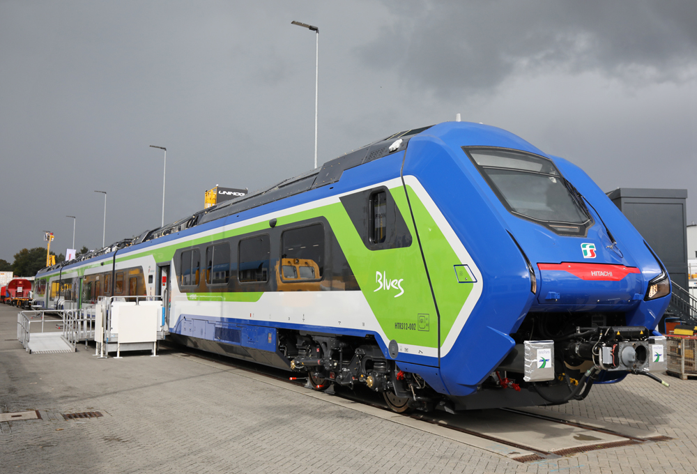 Blue, green, and white multiple-unit passenger trainset on display at trade show.