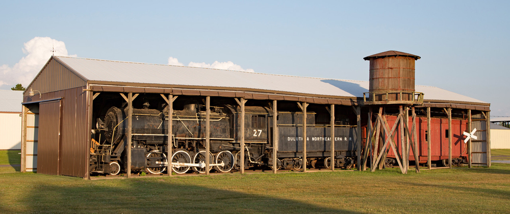 Steam engine and caboose on display in shed open on one side