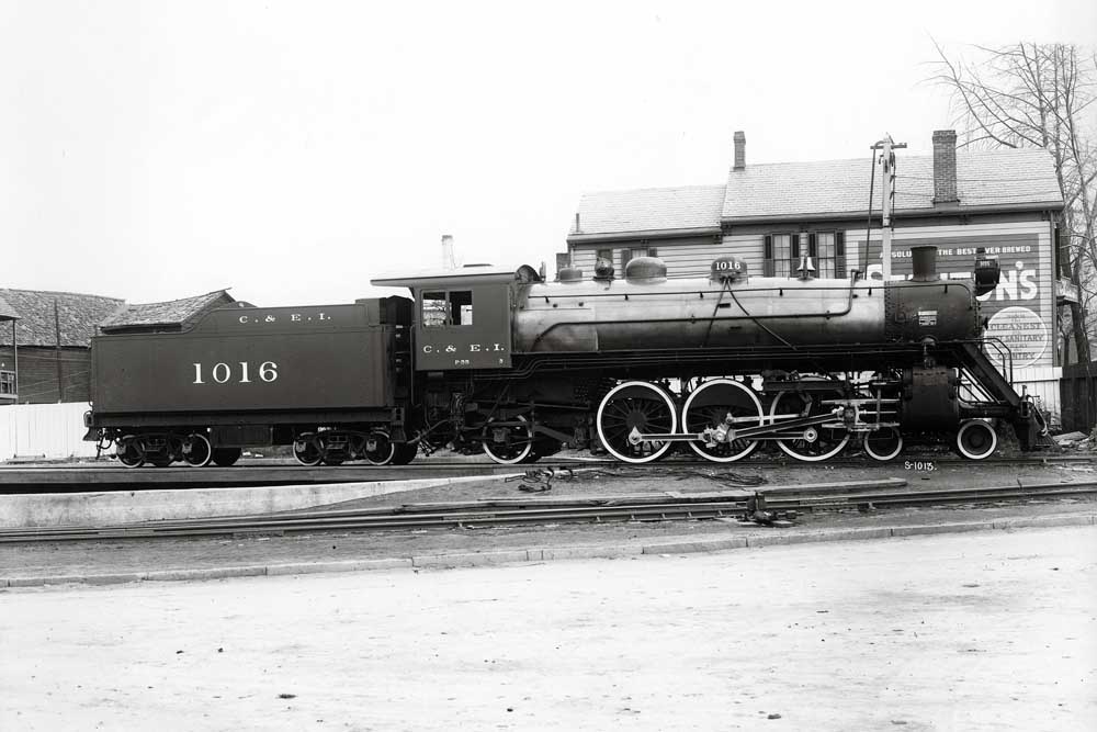 Steam locomotive resting aside wood-frame structure with advertising