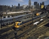 Blue-and-orange streamlined diesel locomotive with passenger train in urban setting