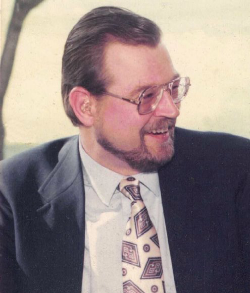 Color photo of man with beard and glasses wearing a sport coat and tie