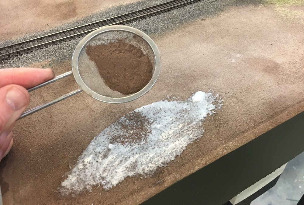 Color image showing tile grout being applied with fine mesh sifter in white glue.