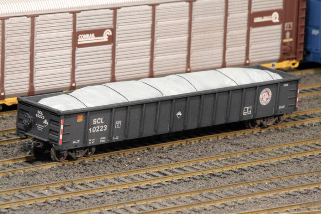 Color photo of black gondola with white plastic tarp covering load.
