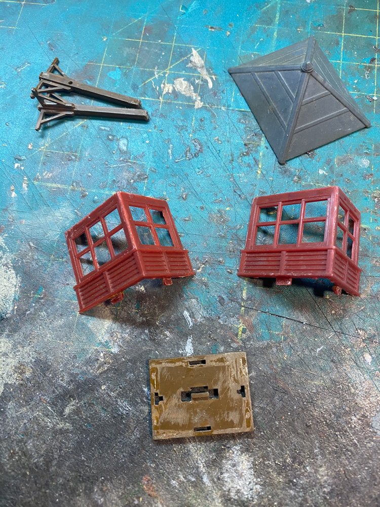 Small gray, red, and tan plastic pieces used to make the Atlas elevated gate tower resting on a well-worn green modeler’s cutting mat.