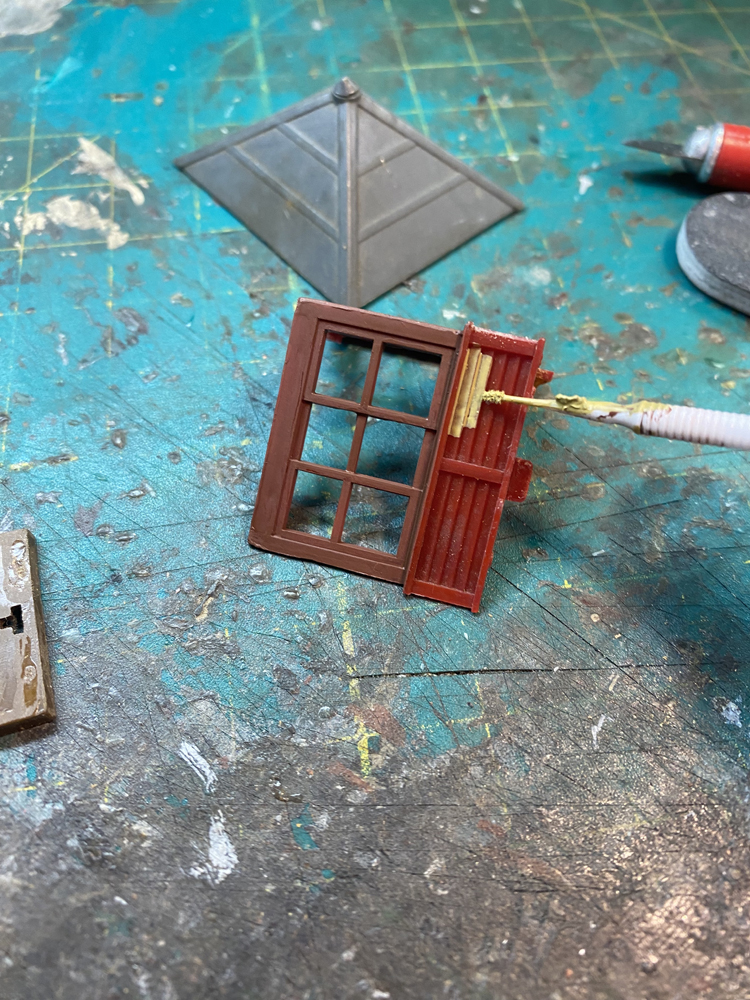 Plastic Atlas elevated gate tower parts with windows painted dark red/brown and a small white paint brush applying light yellow paint to the walls.