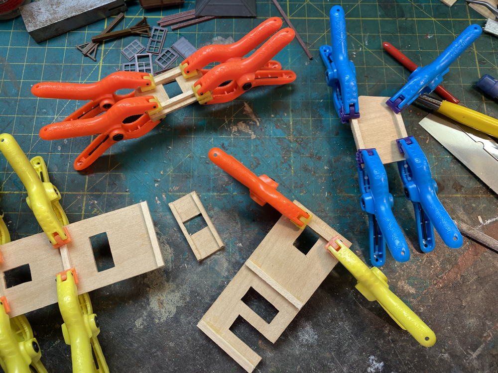 Small rectangular pieces of wood with brightly colored spring clamps resting on a worn, green workbench.