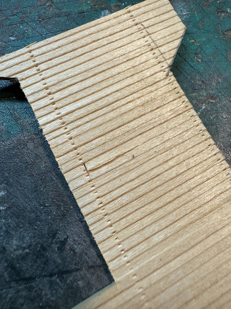 A brown piece of model wood siding with nail hole detail showing one piece of siding cut away from the others.