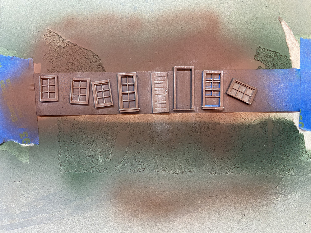 Brown model doors and windows with peeling paint attached to a strip of masking tape.